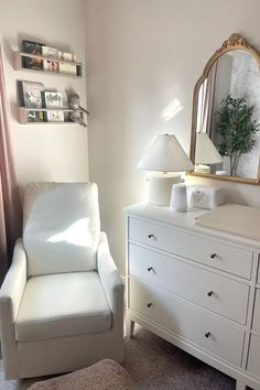 a white chair sitting in front of a dresser next to a mirror on top of a wall