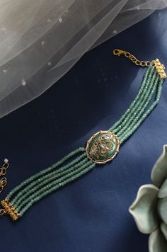 Indulge in elegance with this captivating choker necklace, adorned with exquisite details that set it apart as a unique accessory. Its central focal point showcases an oval jade stone, emitting a soothing mint green hue that exudes tranquility and freshness. The intricate Hauldili work adds delicate patterns and fine detailing, creating a visually appealing contrast against the cool mint green backdrop. Finish: 22KT Gold Plating Material: Silver, Copper Alloy, Onyx, Kundan & Pearl Color: Green S Exquisite Green Jade Jewelry, Green Jade Necklaces For Weddings, Elegant Adjustable Green Choker, Elegant Green Adjustable Choker, Elegant Choker With Natural Stones And Round Beads, Elegant Choker With Round Natural Stones, Oval Jade Necklaces For Wedding, Elegant Green Emerald Necklace Adjustable, Elegant Turquoise Jade Jewelry