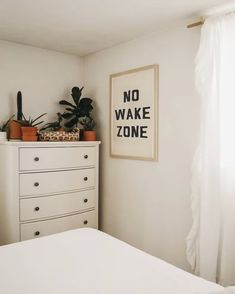 a bedroom with white furniture and plants on top of the dresser in front of a window