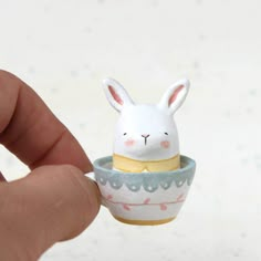 a hand holding a tiny white rabbit in a cup