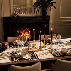 a table set with place settings, plates and candles in front of a fire place