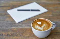 a cup of coffee sitting on top of a wooden table next to a notepad