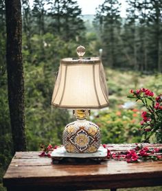 a lamp sitting on top of a wooden table next to a flower filled vase and potted plant