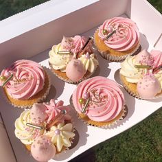 six cupcakes with pink frosting and sprinkles in a box