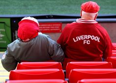 two people sitting on red seats in front of a soccer field with the words liverpool fc written on them