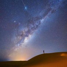 a man standing on top of a sand dune under a night sky