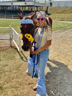 a woman standing next to a brown horse in a fenced in area with sunflowers