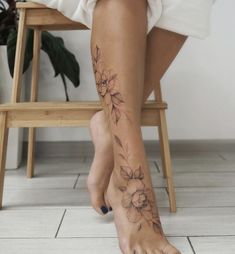 a woman sitting on a chair with her legs crossed and flowers tattooed on the leg