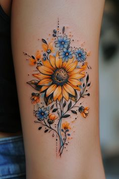 a sunflower tattoo with blue and yellow flowers on the side of a woman's thigh