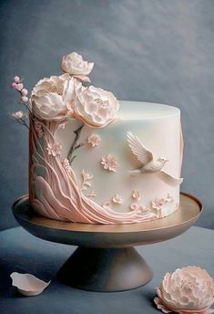 a white cake with pink flowers and birds on the top is sitting on a silver platter