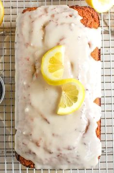 a loaf of lemon bread with icing on a cooling rack next to sliced lemons