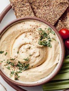 hummus in a bowl with celery, tomatoes and crackers on the side