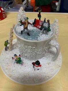 a cup filled with snow and people on top of it, in the middle of a table