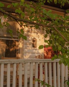 the front porch of a house with a white picket fence and tree branches in front of it