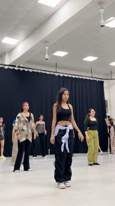 several people are standing in a large room with black drapes on the ceiling and one woman is wearing a white sash around her waist