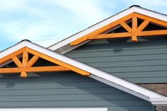 two wooden beams on the roof of a gray and white house with blue sky in the background