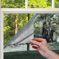 a person holding up a piece of paper in front of a window with trees outside