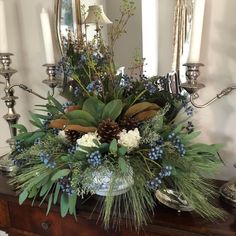 a vase filled with flowers and greenery on top of a table next to candles