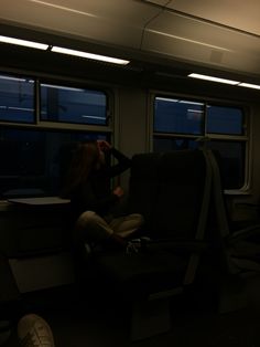 a woman sitting on a train looking out the window at the night time and holding her head