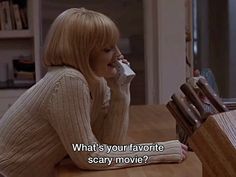 a woman sitting at a table drinking from a cup with the caption what's your favorite scary movie?