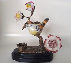 a statue of a bird sitting on top of a tree branch next to a flower