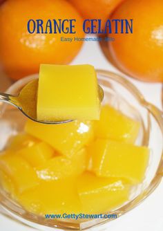 orange gelatin is being spooned into a glass bowl filled with cubed mangoes