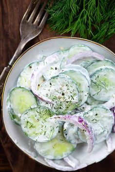 cucumber salad in a white bowl with dill and onions on the side