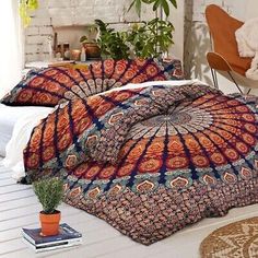 a bed with an orange and blue comforter on top of it next to a plant