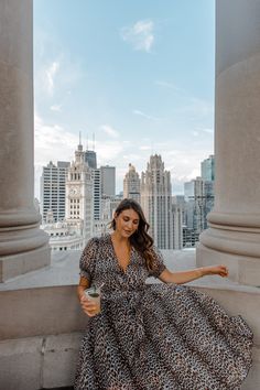 a woman in a leopard print dress is sitting on some pillars and holding a cup