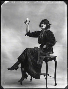 an old photo of a woman sitting on a chair holding a cup