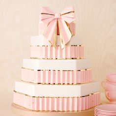 a three tiered cake with pink bows on top and plates next to it in front of a wall