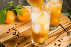 orange juice being poured into glasses on a cutting board with an orange in the background