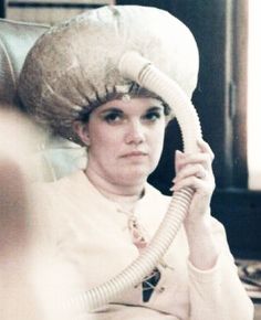 a woman wearing a white hat and holding a telephone to her ear while sitting in a chair