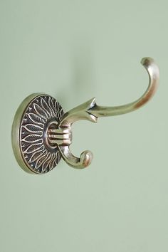 a metal hook with a decorative design on it's end, hanging from a green wall