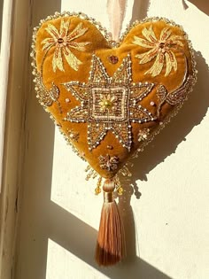 a heart shaped decoration hanging on the side of a building with beads and tassels