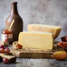 two slices of cheese sitting on top of a wooden cutting board next to some grapes