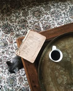 a cat is looking down at a table with a book and coffee cup on it