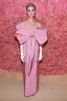 a woman in a pink dress standing next to a wall with red flowers on it