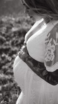 black and white photograph of a pregnant woman in a field with flowers on her arm