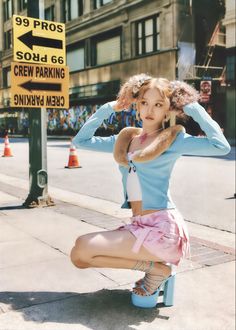 a woman sitting on top of a blue trash can in front of a street sign