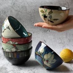 a hand holding a bowl with five different bowls in front of it and a lemon next to it