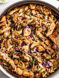 a skillet filled with chicken, cabbage and carrots on top of a table