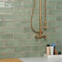 a bathroom with green tiled walls and white counter tops, including a shower head in the corner