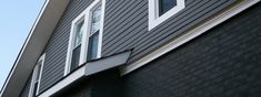 the side of a house with black siding and white trim on it's windows