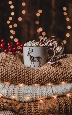 a coffee cup filled with marshmallows on top of a blanket next to candy canes