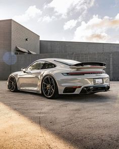 a silver porsche sports car parked in front of a building with the sun shining on it's roof