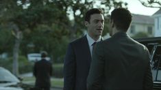 two men in suits are talking to each other near a car parked on the street