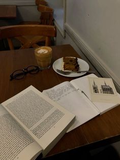 an open book sitting on top of a wooden table next to a slice of cake