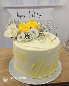 a white cake with yellow flowers and a happy birthday sign on it's side