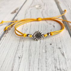 a yellow string bracelet with a silver flower on it, sitting on a wooden surface